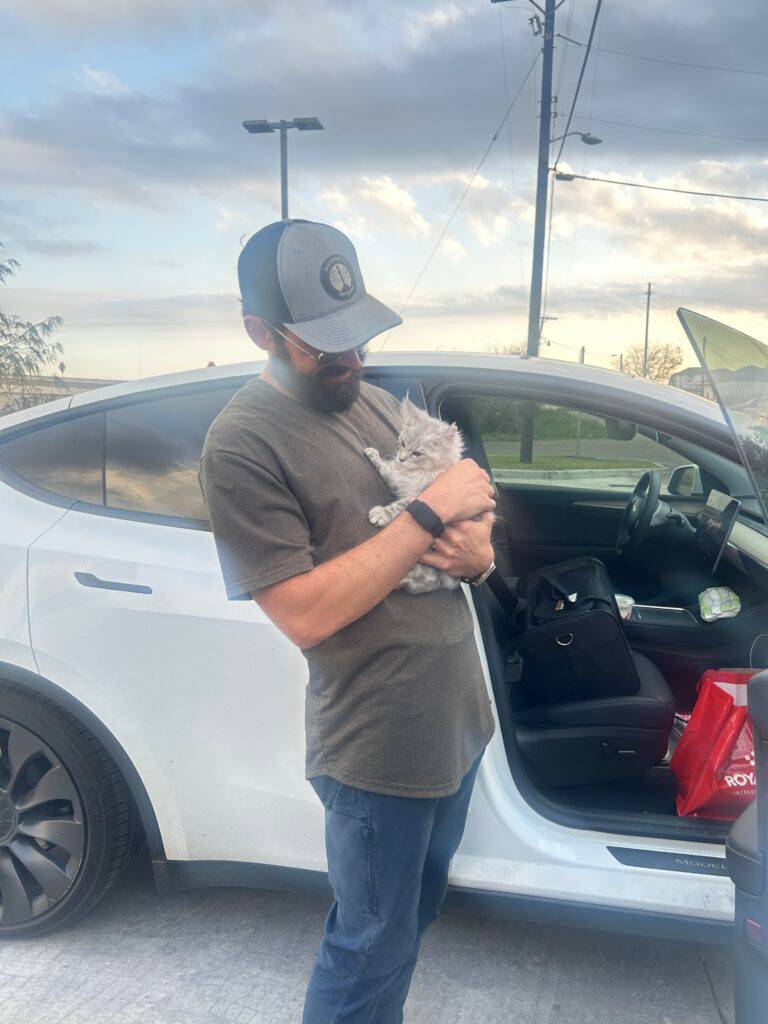 New owner holding his silver Maine Coon kitten beside his car after a midpoint meetup in Kingsville, Texas