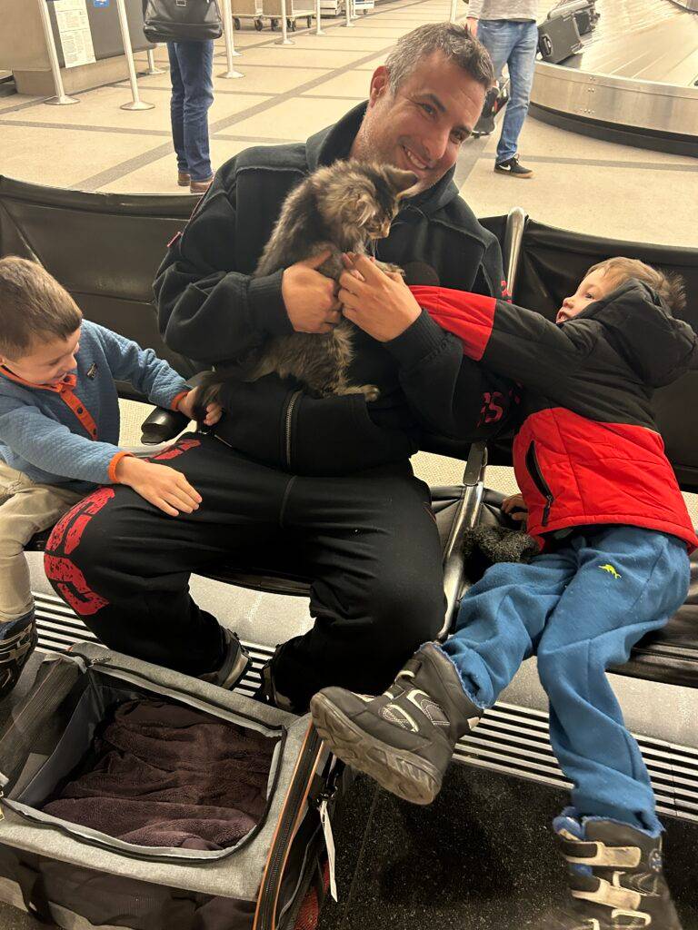 A father holding his new Maine Coon kitten as his two young children meet it for the first time at Jeppesen Terminal, Denver International Airport